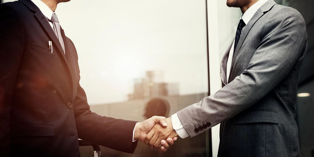 real estate agent shaking hands with client in front of house with 'Sold' sign, wearing masks